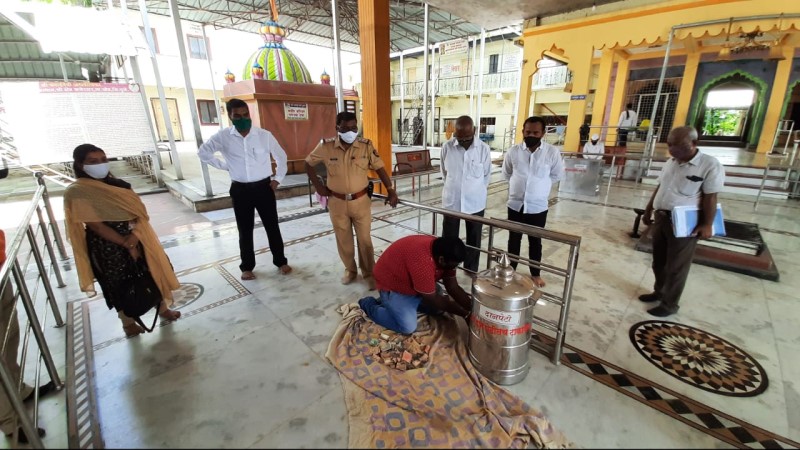 दानपेटीतील रक्कम धातूच्या भांड्यात गोळा करताना; अधिकारी व इतर उपस्थित